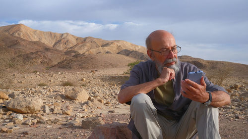 Side view of man sitting on rock against mountain