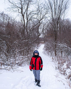 Kid walking along a trail in a forest covered with snow looking at the camera