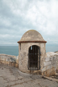 Old building by sea against cloudy sky