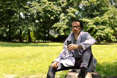 Young man sitting on grass against trees