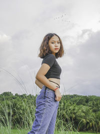 Young woman standing on field against sky