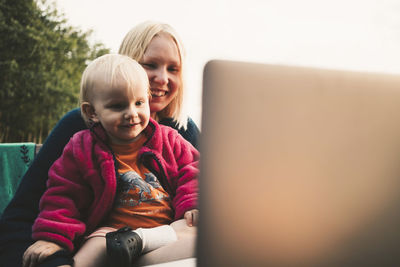 Smiling mother and daughter looking at laptop during video conference on sunny day