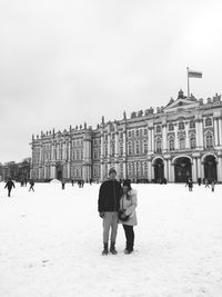 Portrait of couple standing on snow covered field against government building