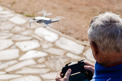 Rear view of the elderly man piloting the drone looking at the remote control display while standing