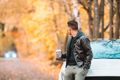 Man holding camera while standing by tree during autumn