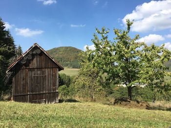 Hut on field by trees against sky