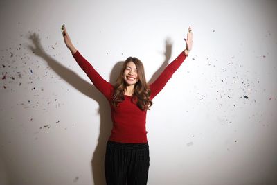 Rear view of woman with arms raised standing against wall