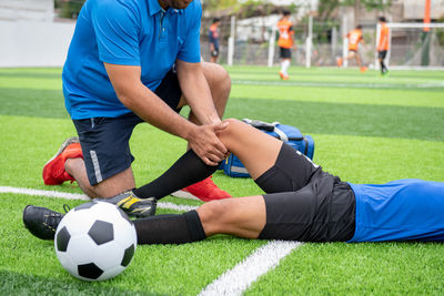 Low section of male physical therapist rubbing soccer player knee on field