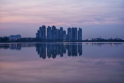 Reflection of buildings in lake against sky during sunrise