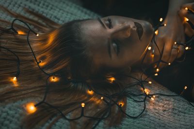 Close-up of young woman lying with illuminated lighting equipment