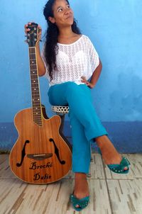 Woman holding guitar while sitting on stool by wall