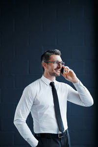 Businessman talking on phone against wall