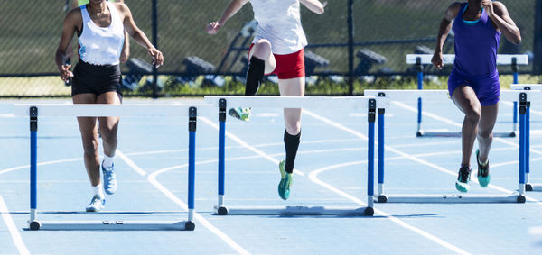 Three high school girls are racing in a 400 meter hurdle race on an outdoor track at a compeition.