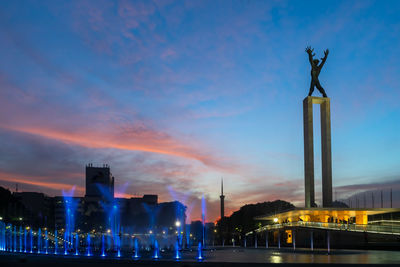 Statue in city against sky at sunset