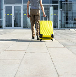 Man traveler in casual carrying yellow suitcase next to entrance to airport outside tourism vacation