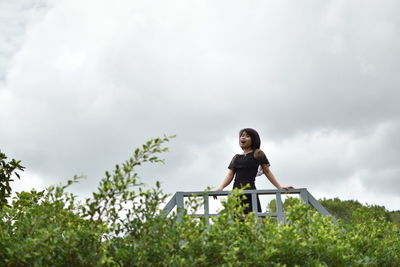 Low angle view of woman standing amidst plants against sky