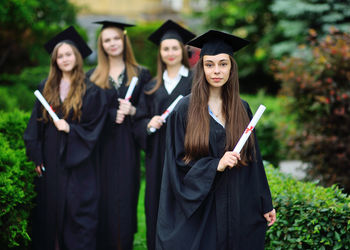 Portrait of smiling young woman wearing graduation gown standing in forest