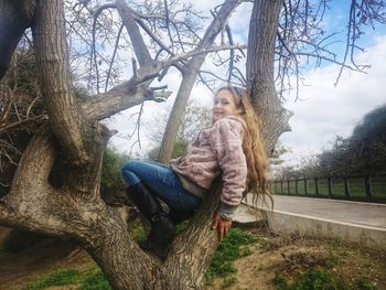 Young woman sitting on tree trunk against bare trees