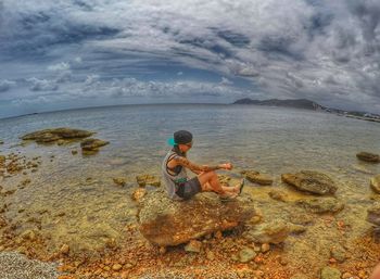 Woman sitting on beach against sky