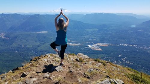 Rear view of woman standing on rock against sky