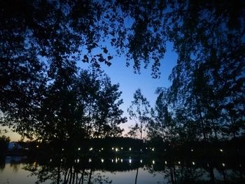 Silhouette trees by lake against sky at night