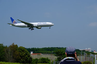 Rear view of man with airplane flying against sky