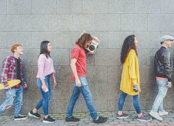 Side view full length of friends walking by wall