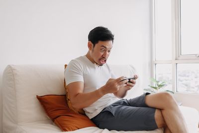 Young man using mobile phone while sitting on bed at home