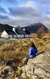 Rear view of woman sitting on rock against sky