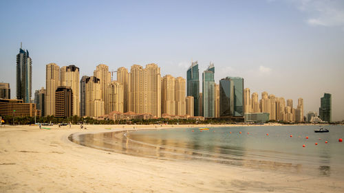 Sea by modern buildings against sky in city