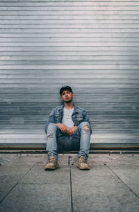 Portrait of young man sitting on footpath