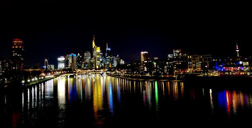Illuminated buildings by river against sky at night
