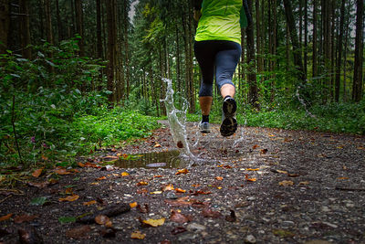 Low section of person running on street amidst trees in forest