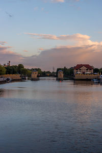 River by buildings in city against sky during sunset