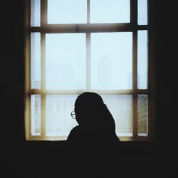 Silhouette woman looking through window at home