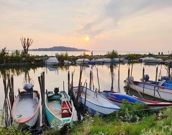 Boats moored in lake against sky during sunset