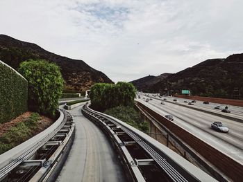 Tram tracks by highway against sky