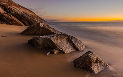 Rock formations at sea shore against sky during sunset