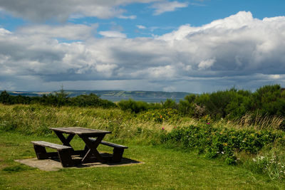 Empty picnic table and bench on shore by sea against sky