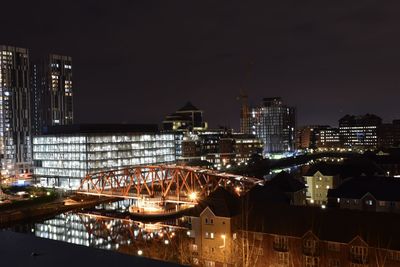 Illuminated buildings by river against sky at night