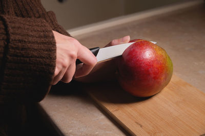 The hand holds a fresh mango. fresh ripe organic mango. woman cutting mango on wooden cutting board