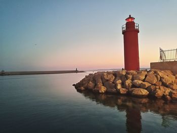 Lighthouse by sea against sky during sunset