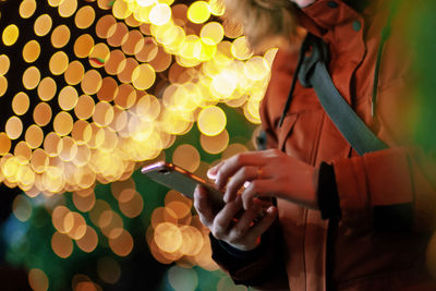 Midsection of woman holding illuminated lighting equipment at night
