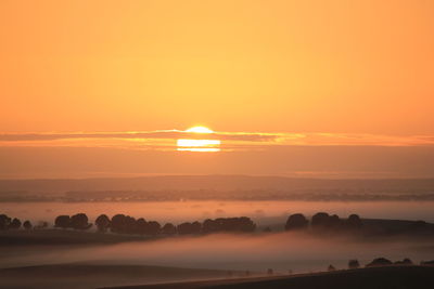 Scenic view of landscape in foggy weather against orange sky during sunset