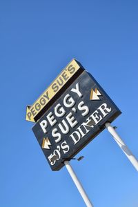 Low angle view of road sign against clear blue sky