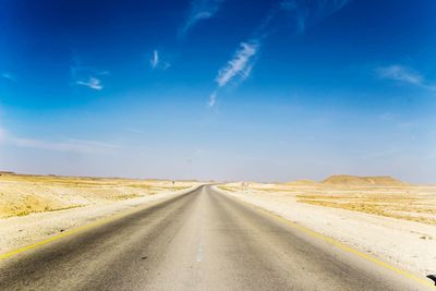 Empty road amidst land against blue sky