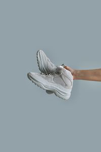 Cropped hand of person holding shoes against gray background