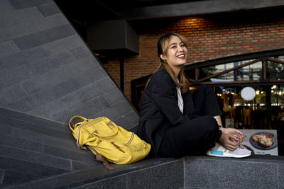 Portrait of smiling businesswoman with backpack sitting on retaining wall