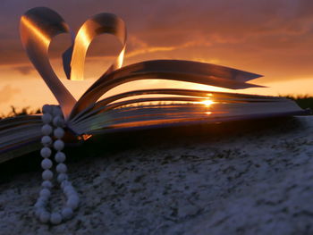 Bead necklace with heart shape folded pages of book during sunset