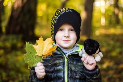 Portrait of cute boy holding autumn leaves and stuffed toy